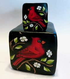 two red birds sitting on top of black boxes with flowers and leaves painted on them