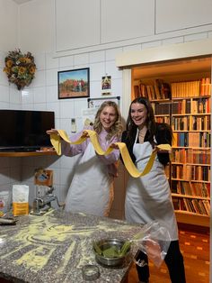 two women in aprons are holding yellow ribbon at the end of a kitchen counter