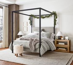 a bedroom with a canopy bed and white carpeted flooring in front of large windows