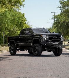 a large black truck parked on the side of a road next to trees and bushes