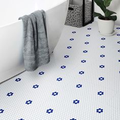 a white bath tub sitting next to a plant in a bathroom on top of a tiled floor