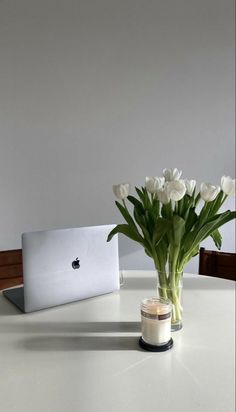 a vase filled with white flowers sitting on top of a table next to a laptop computer