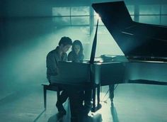 a man and woman sitting at a piano in front of a window with light streaming through it