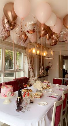 the table is set for a party with pink and gold balloons hanging from the ceiling