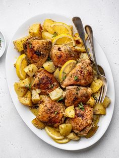 a white plate topped with chicken, potatoes and lemon wedges next to a fork