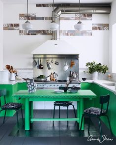 a kitchen with green tables and chairs in it's center island, surrounded by hanging pots and pans