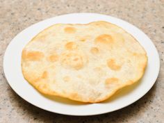 a white plate topped with a flat bread on top of a marble countertop next to a knife and fork