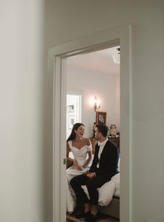 a man and woman sitting on top of a bed in front of a doorway together