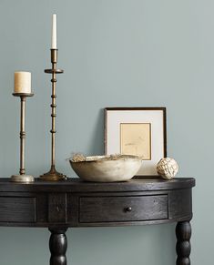 a wooden table topped with a bowl and two candles next to a framed photograph on the wall