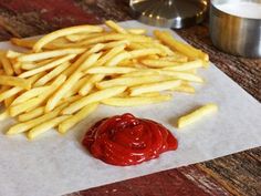 french fries with ketchup on the side sitting on wax paper next to a can