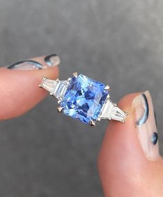 a woman's hand holding an engagement ring with blue and white stones