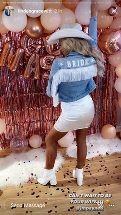 a woman standing in front of balloons wearing a cowboy hat and fringed denim jacket