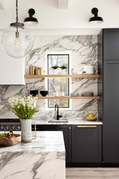 a kitchen with marble counter tops and black cabinets, along with hanging lights above the sink