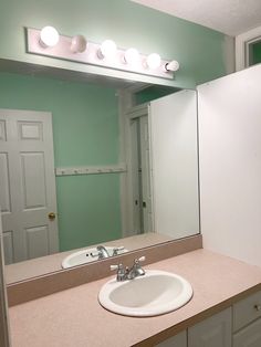 a bathroom sink sitting under a mirror next to a white door and light on the wall