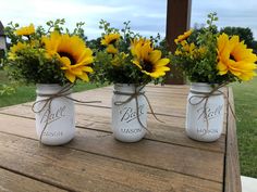 three mason jars with sunflowers tied to them sitting on a picnic table outside