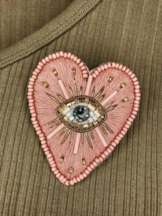 a pink heart shaped brooch with an eye in the center and beads around it