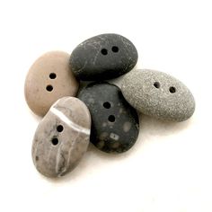 five different colored rocks with holes in them on a white surface, one is black and the other is gray