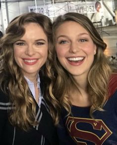 two women are posing for the camera in front of a sign that says supergirl