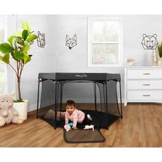 a baby sitting in a playpen on the floor next to a potted plant