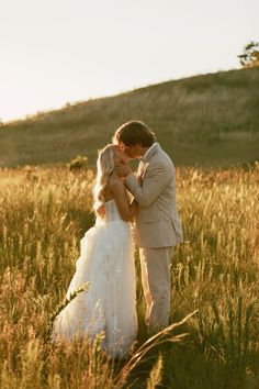 a bride and groom kissing in the middle of a field with tall grass at sunset