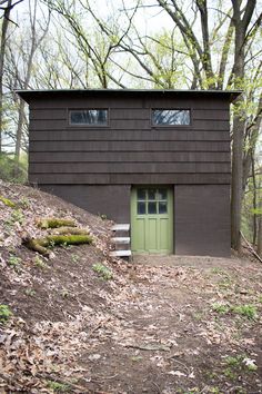 a small house with a green door on top of a hill in the woods next to some trees