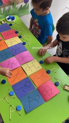 two children are playing with letters and numbers made from construction paper on a table in front of them