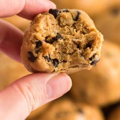 a hand holding up a cookie in front of a pile of other muffins