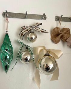 three ornaments hanging on a wall with ribbons and bells attached to the pegs in front of them