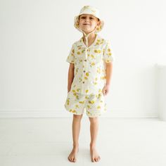 A young toddler stands barefoot in a light, airy room, wearing a Makemake Organics Organic Linen Shirt and Shorts Set adorned with lemon prints. The child looks directly at the camera with a subtle smile. Cotton Sleepover Sets For Summer, Summer Cotton Sleepwear, Cotton Summer Sleepwear, Summer Cotton Sets For Sleepovers, Cotton Summer Sets For Sleepover, Summer Cotton Sleepover Sets, Summer Sleepover Short Sleeve Sets, Playful Cotton Short Set For Summer, Cotton Short Sleeve Short Set For Vacation