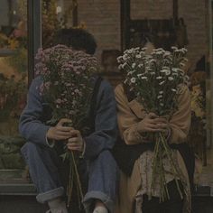 two people sitting on the ground with flowers in front of their faces, one holding his head