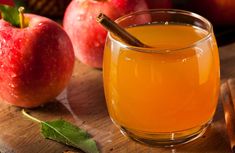 an apple cider with cinnamon stick in it next to apples on a wooden table