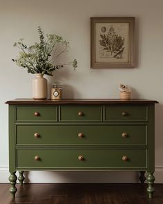 a green dresser with two vases on top of it next to a framed painting