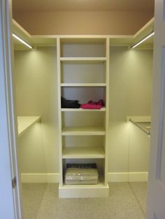 an empty walk in closet with white shelving and lights on either side of the door