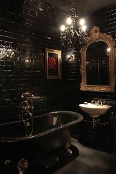 a bathroom with black tile walls and a claw foot bathtub in the center, along with a chandelier