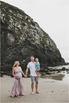 a man and woman holding hands while walking on the beach with a baby in their arms