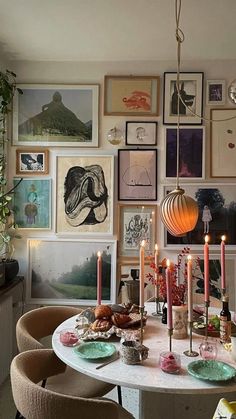 a dining room table with candles and pictures on the wall above it, surrounded by chairs