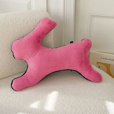 a pink dog bone pillow sitting on top of a white couch