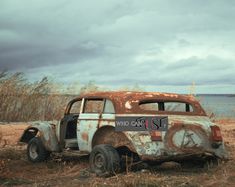 an old rusted out car sitting on the side of a road next to water