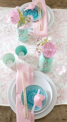 the table is set with pink and blue plates, napkins, and flowers in vases