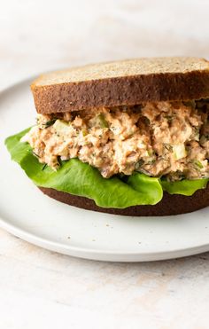 a sandwich with lettuce and tuna on it sitting on top of a white plate