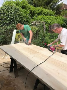 two men working on a wooden table with power tools in their hands and an electric sanding machine next to them