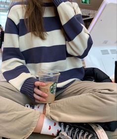 a woman sitting on the ground holding a cup of coffee