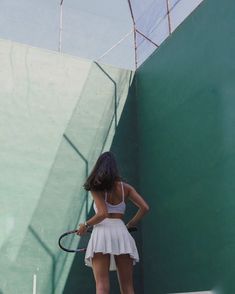 a woman holding a tennis racquet on top of a tennis court in front of a green wall