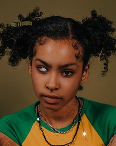 a young woman with black hair wearing a green and yellow t - shirt looking at the camera