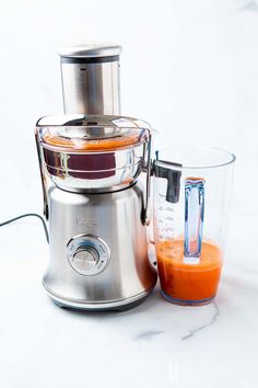 a blender sitting on top of a white counter next to a glass filled with orange juice