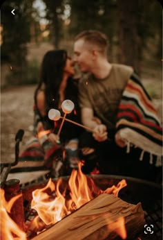 a man and woman sitting in front of a fire with marshmallows on it