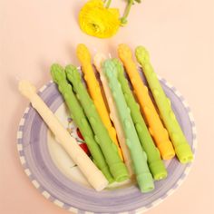 four different colored candles sitting on top of a purple and white plate next to yellow flowers