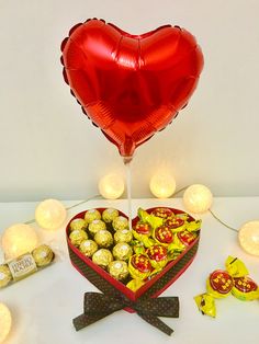 a heart shaped box filled with chocolates next to a balloon and some candies