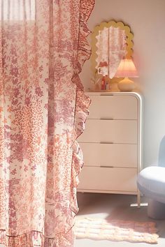 the curtains in this room are pink and white with flowers on them, along with a blue chair