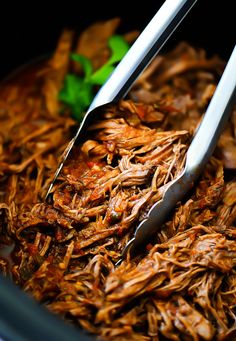 two tongs sticking out of shredded meat in a bowl